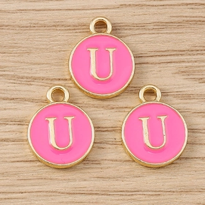 Macro detail of three pink enamel and gold letter U charms on light wood texture background