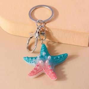 Macro shot of gradient resin starfish keychain with silver metal clasp on sand display