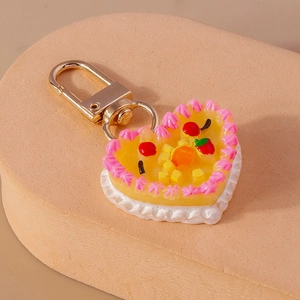Macro side view of a heart-shaped fruit cake keychain with pink cream and gold metal clasp