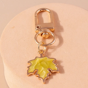 Detailed view of a golden maple leaf keychain with yellow enamel texture on a stone stand