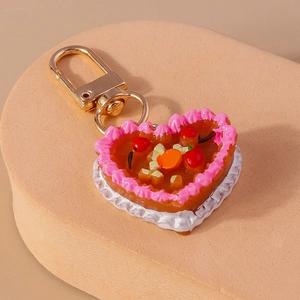 Detail view of heart-shaped fruit cake keychain with pink cream and gold rotating clasp