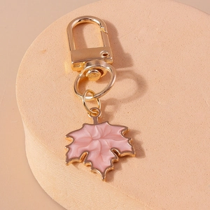 Detail view of pink maple leaf pendant with golden lobster clasp on a stone surface