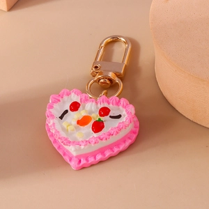 Detail of heart cake keychain with pink cream, red cherry, and golden lobster clasp