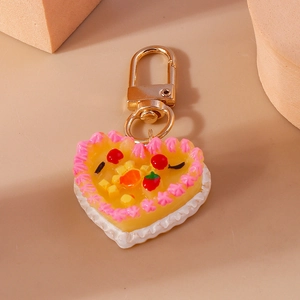 Macro detail of a heart-shaped cake keychain with yellow icing and strawberry topper