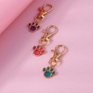 Three gold alloy pet paw pendants with colorful enamel drips on pink background