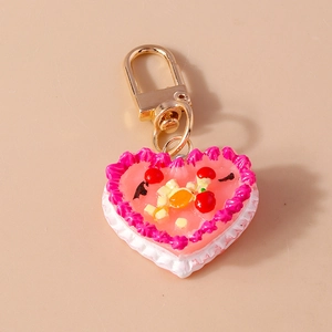 Detail of a pink heart cake keychain with cream texture and realistic fruit toppings