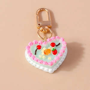 Detail of heart-shaped cake keychain with pink cream frosting and miniature fruit pieces