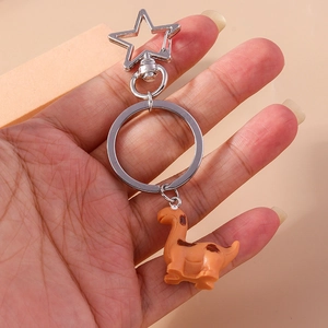 Hand holding a cute orange dinosaur keychain with silver star carabiner on pink background