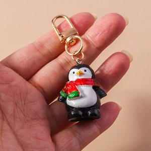 Primer plano de un llavero de pingüino de resina con bufanda sostenido para ver tamaño