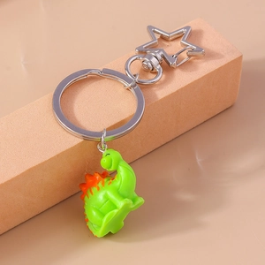 Close-up of cute green cartoon dinosaur keychain with orange spines and star-shaped clip