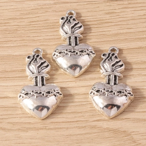 Detailed view of three silver sacred heart pendants with crown of thorns and flame on wood