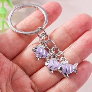 Porte-clés poisson rayé violet mignon avec anneau en métal argenté tenu dans la main