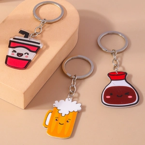 Three cute cartoon acrylic beverage keychains including beer and soda on beige display