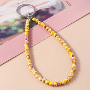 Portachiavi alla moda con perle marmorizzate gialle e anello argento su fondo beige