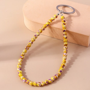 Dettaglio del portachiavi con perline gialle e viola e anello in metallo su supporto curvo