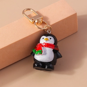 Detalle de llavero de pingüino navideño con bufanda y cierre de mosquetón dorado