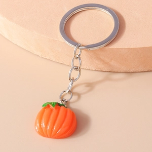 Close-up of orange pumpkin keychain with green leaves and silver ring on beige podium