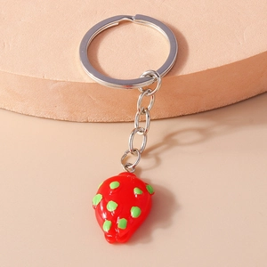 Detail of a red strawberry keychain with green seeds on a pink pedestal