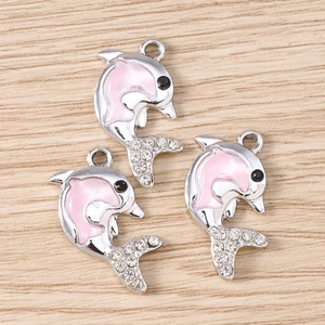 Tre ciondoli a delfino argento con smalto rosa e strass bianchi su fondo legno