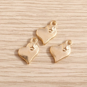 Trois breloques cœur dorées avec relief de fleur de camélia sur fond de bois clair