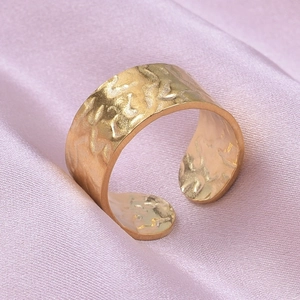 Detailed close-up of wide golden stainless steel ring with hammered texture and open band