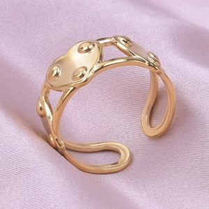 Detail of a gold heart adjustable ring with dot texture on a pink silk background