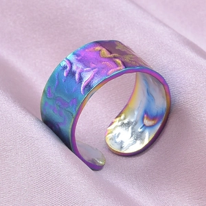 Detail of rainbow gradient stainless steel ring with hammered texture on pink satin