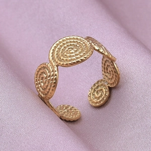 Detail view of golden spiral textured disk ring on soft purple silk fabric