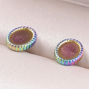 Détail de boucles d'oreilles ovales arc-en-ciel avec relief brun-rouge sur velours beige doux