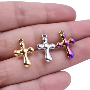 Détail de pendentifs croix en acier inoxydable or et argent tenus en main pour bijoux DIY