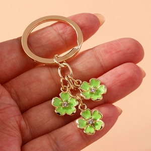 Detail of a golden metal keychain featuring three green enamel five-leaf flower pendants