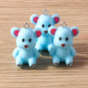 Three light blue resin bear pendants with silver metal loops on a wood background