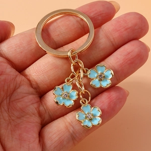 Detail of hand holding gold keychain with three light blue enamel five-petal flowers