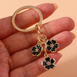 Detailed close-up of golden alloy keychain featuring three black enamel flower charms