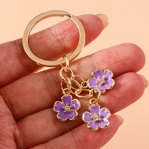 Handheld view of elegant purple flower keychain with golden plating and enamel petals