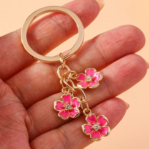 Detailed macro view of gold keychain with three pink enamel flowers and tiny crystals