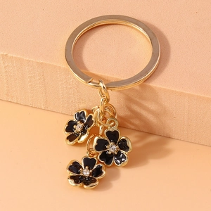 Close-up of black enamel flower keychain charms with gold metal edges and rhinestones
