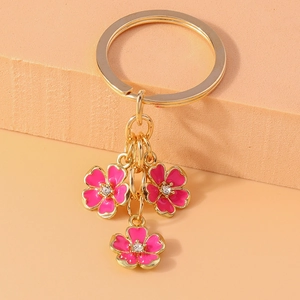 Detailed close-up of golden keychain with three pink enamel flowers and crystal accents