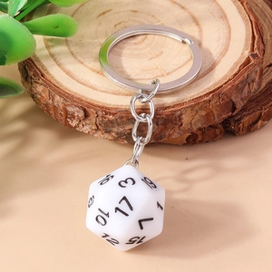 Detailed close-up of a white D20 dice keychain with black numbers on a wooden coaster
