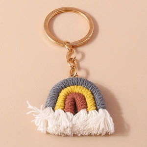 Handmade rainbow woven keychain with cotton ropes and soft white tassels on pink surface