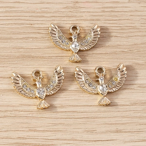 Three gold eagle bird charms with crystal rhinestones on a light wood background