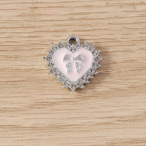 Detail van roze geëmailleerde hartvormige hanger met zilveren strik en strasstenen