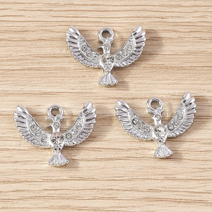 Three silver-plated eagle charms with sparkling white rhinestones on wooden surface