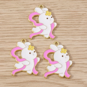 Detailed macro view of three rabbit enamel charms with pink ribbons on wood surface