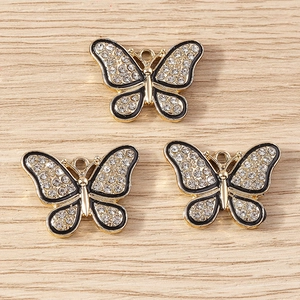Trois pendentifs papillon en alliage doré avec émail et strass sur fond de bois