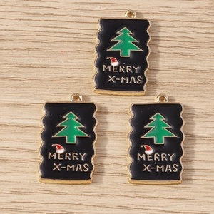 Close-up of three Christmas tree enamel charms with Merry X-mas text on wood background