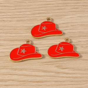 Macro view of three red enamel cowboy hat charms with gold star details on wood surface