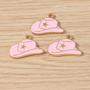 Pink enamel cowboy hat pendants with gold star accents on light wood background