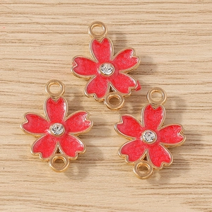 Three pieces of cherry blossom jewelry connectors with red enamel and crystals on wood