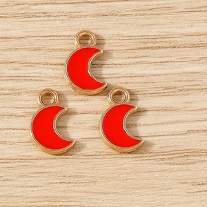 Three red enamel crescent moon pendants with gold alloy plating on light wood background